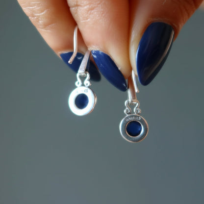 Silver earrings with blue stones held by a hand with blue nail polish on a gray background